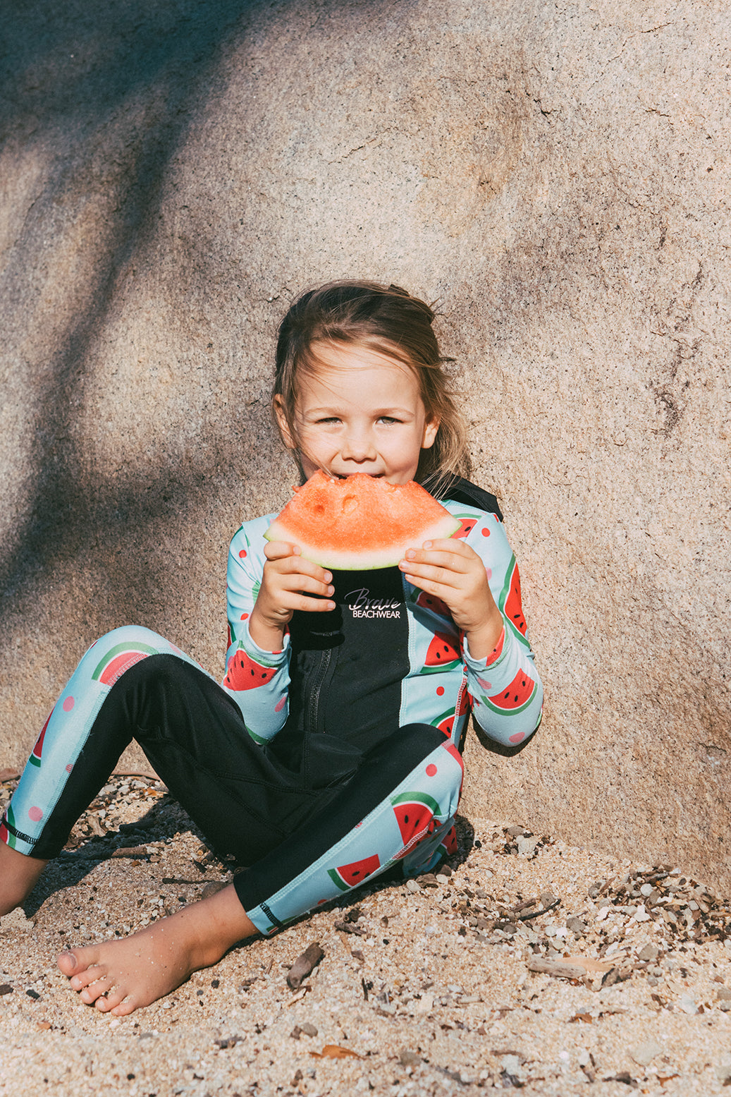 Girl eating a watermelon on the beach in a Brave stingersuit