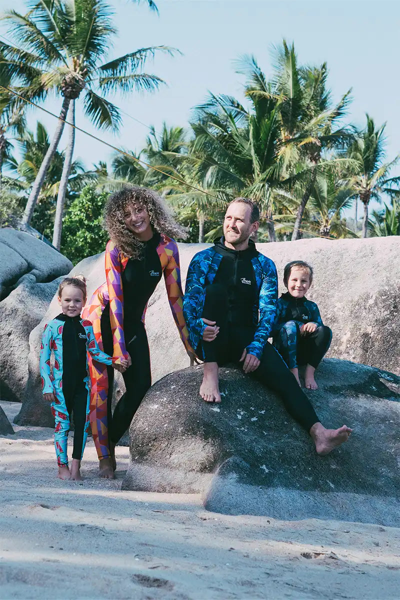 Family in stingersuits sitting on rock at the beach happy